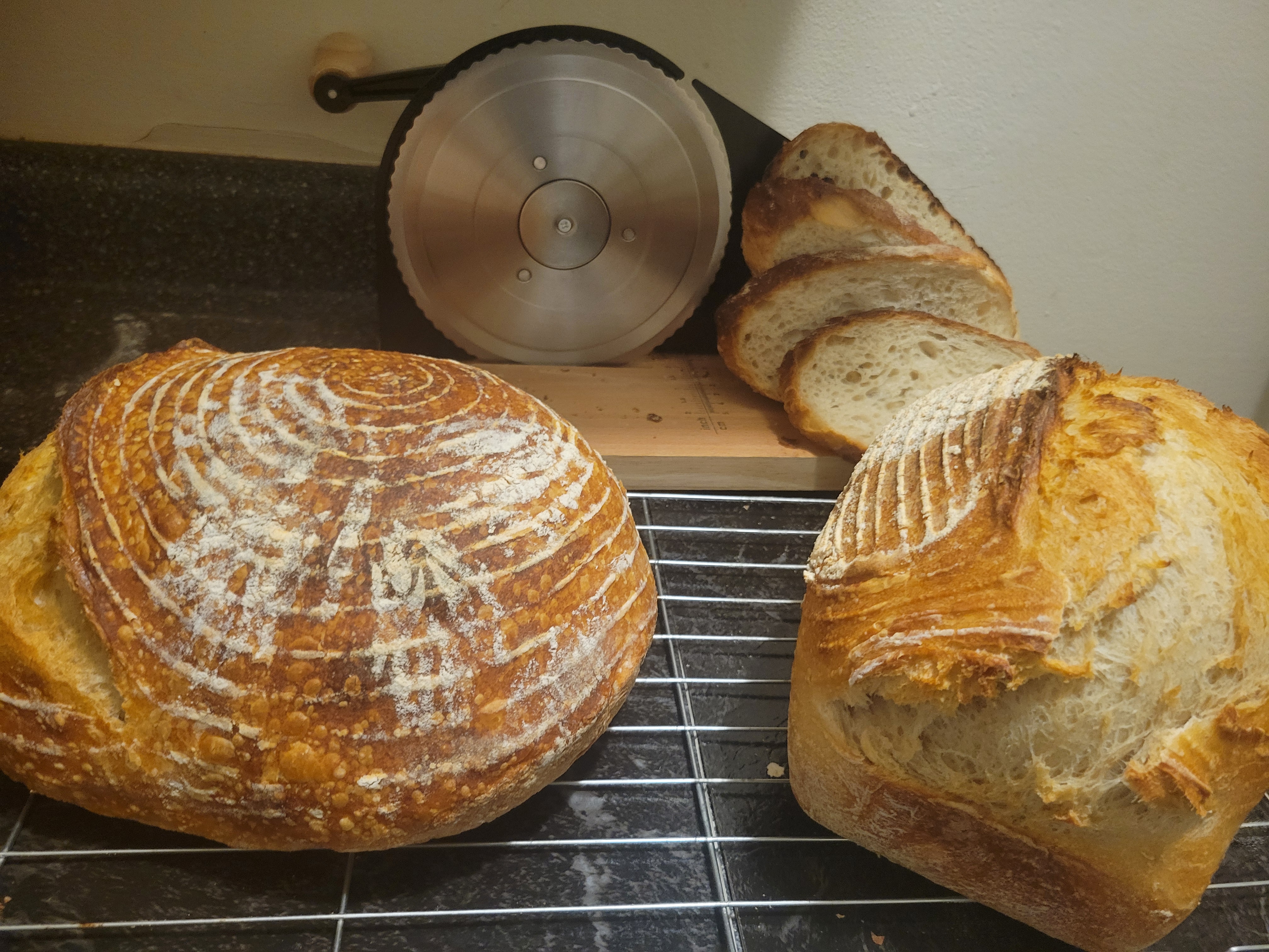 two whole sourdough loaves with a sliced portion displayed behind.